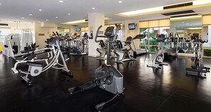 A gym with multiple cardio machines, including treadmills and elliptical trainers, arranged in rows.