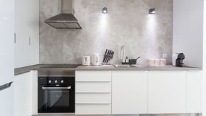 A modern kitchen with a built-in oven, a range hood, and a countertop with a coffee maker, knife block, and storage containers. - Central & Spacious 2BR in Almada • Easy access to Lisbon (Almada)