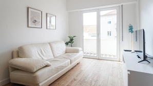 A modern living room with a beige sofa, a flat-screen TV, and a sliding glass door leading to an outdoor area. - Central & Spacious 2BR in Almada • Easy access to Lisbon (Almada)
