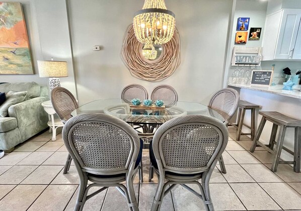 A dining area with a glass table surrounded by wicker chairs, a decorative chandelier, and a wall-mounted light fixture.