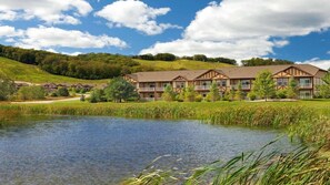 Um hotel com um edifício grande, um lago e uma paisagem montanhosa ao fundo.