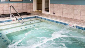 Uma banheira de hidromassagem com escada de metal, paredes azulejadas e piscina azul cristalina.