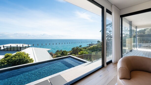 Ein modernes Zimmer mit großem Fenster mit Blick auf einen Swimmingpool und das Meer.