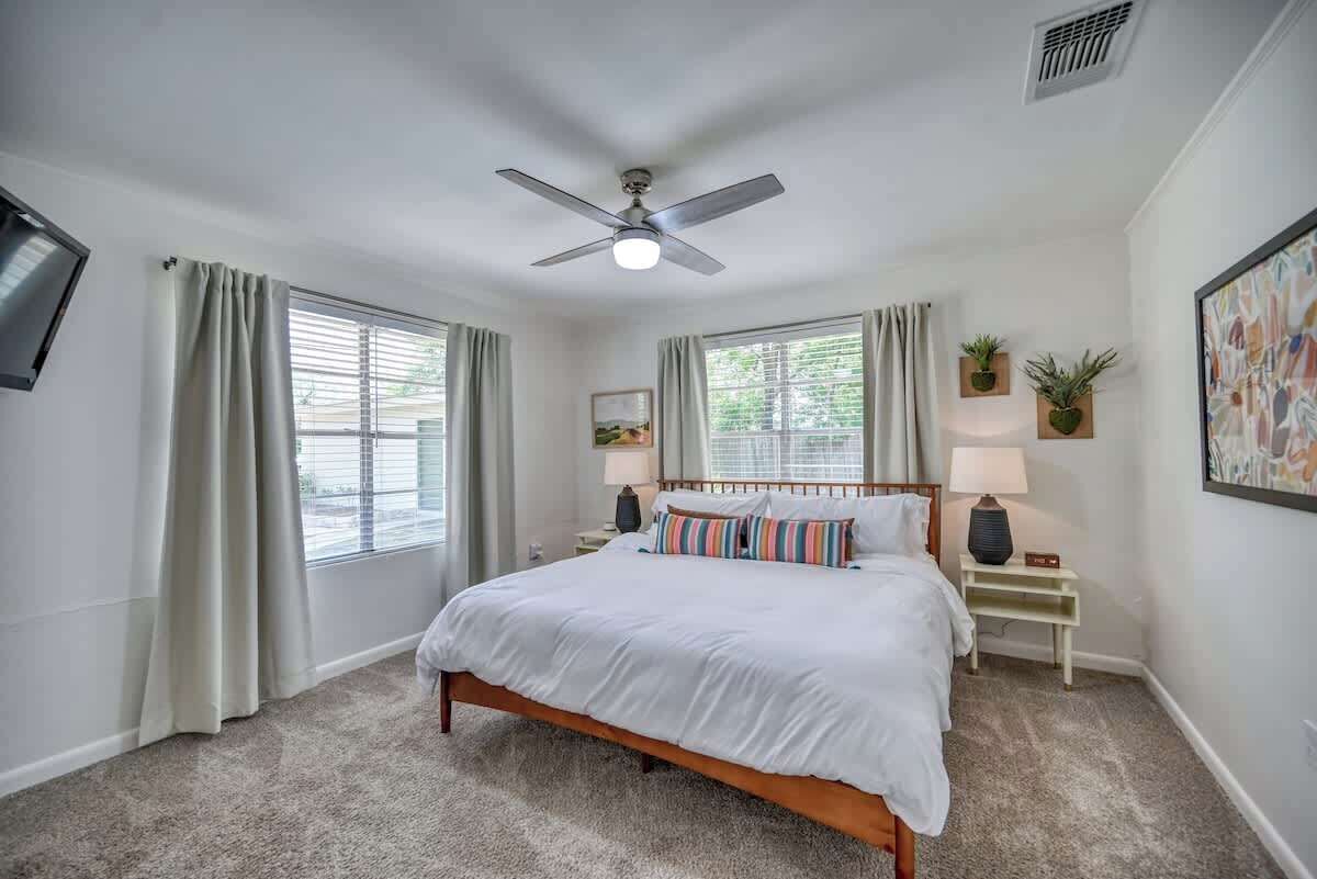 A bedroom with a bed, a ceiling fan, two bedside tables with lamps, and a window with curtains.