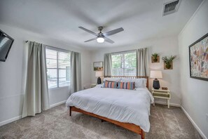 A bedroom with a bed, a ceiling fan, two bedside tables with lamps, and a window with curtains.