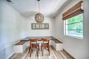 Zona de dinar amb taula, dues cadires, un senyal que diu "SWIM" i una finestra amb vista a vegetació.