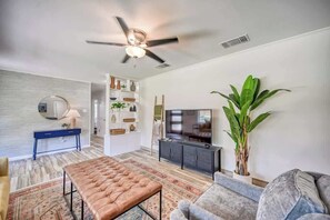 A modern living room with a ceiling fan, a television, a large plant, and a patterned rug. - Lakefront Near Schlitterbahn and New Braunfels (McQueeney)