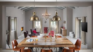 A spacious dining area with a large wooden table, leather chairs, and two hanging brass chandeliers.