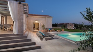 A poolside area with a stone building, outdoor seating, and a clear view of the sky.
