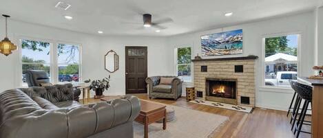 A spacious living room with a fireplace, leather sofa, and a large window.