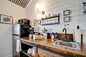 A kitchen with a wooden countertop, stainless steel sink, and a microwave. There are framed pictures on the wall and a sign indicating a septic system.
