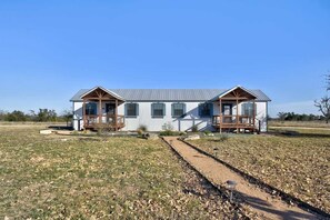 A modern two-story house with a covered porch on each side, a gravel driveway, and a clear blue sky.