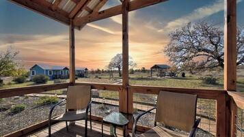 A wooden deck with chairs and a table, overlooking a rural landscape with houses and trees.