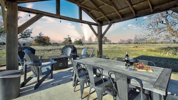 Un patio al aire libre con mesa y sillas de madera, una parrilla y una vista panorámica del campo.