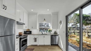 Une cuisine moderne avec des armoires blanches, des appareils en acier inoxydable et une grande fenêtre donnant sur l’extérieur.