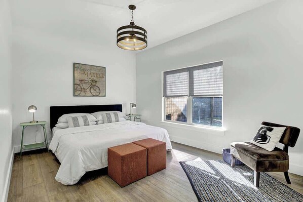 A bedroom with a bed, a nightstand, a bench, a window, and a hanging light fixture.