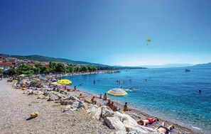 A beach with people sunbathing and swimming, a boat in the water, and a clear blue sky.