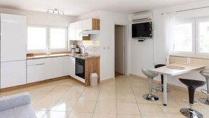 A modern kitchen with white cabinets, a wooden countertop, and a built-in oven. There is a small dining area with a table and bar stools. - 1 bedroom beautiful apartment in Crikvenica (Crikvenica)
