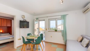 Un espace de vie compact comprenant un coin repas, un canapé, un téléviseur fixé au mur et une vue par la fenêtre.