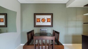 A dining area with a glass-top table, wooden chairs, and a framed artwork on the wall. - Apto 2 Qtos c/ Churrasq. a 650m da praia ESP0301 (Florianópolis)