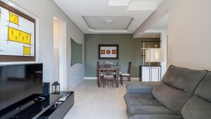 A modern living room with a flat-screen TV, a sofa, a dining area with chairs, and a ceiling with recessed lighting. - Apto 2 Qtos c/ Churrasq. a 650m da praia ESP0301 (Florianópolis)