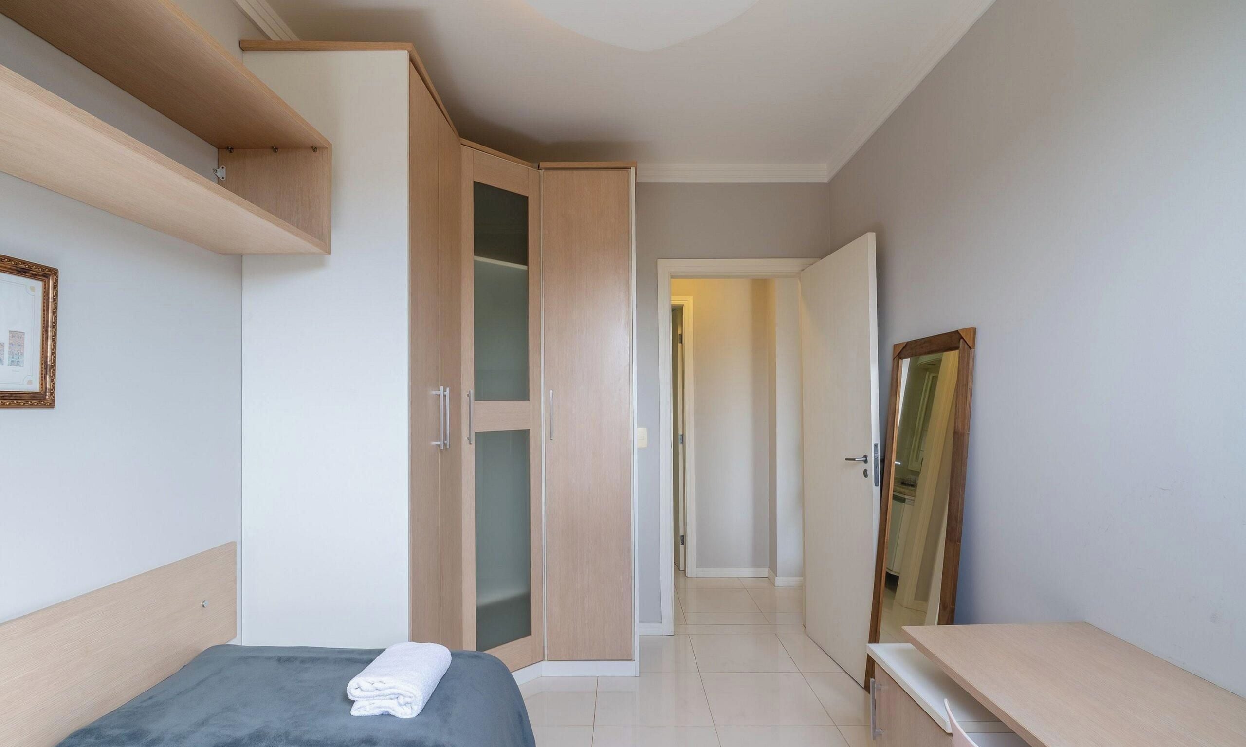 Un dormitorio con cama, armario, espejo y un pasillo que conduce a otra habitación.