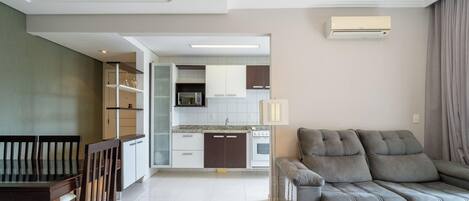 A modern living room with a grey sofa, a dining table with chairs, and a kitchen area in the background.