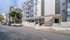 A modern apartment building with a flat facade, multiple balconies, and a parking area with several cars. - Apto 2 Qtos c/ Churrasq. a 650m da praia ESP0301 (Florianópolis)