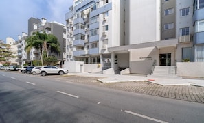 Um edifício de apartamentos moderno com fachada plana, várias varandas e uma área de estacionamento com diversos carros.