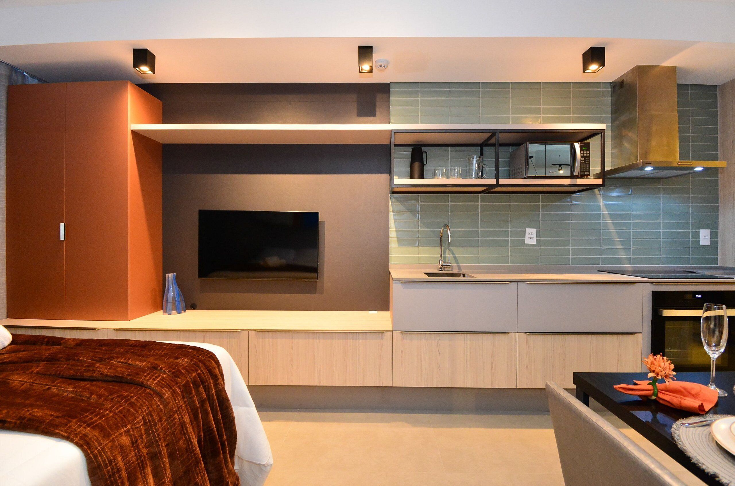 A modern hotel room with a flat-screen TV, a small kitchen area with a microwave, and a dining table set for two.