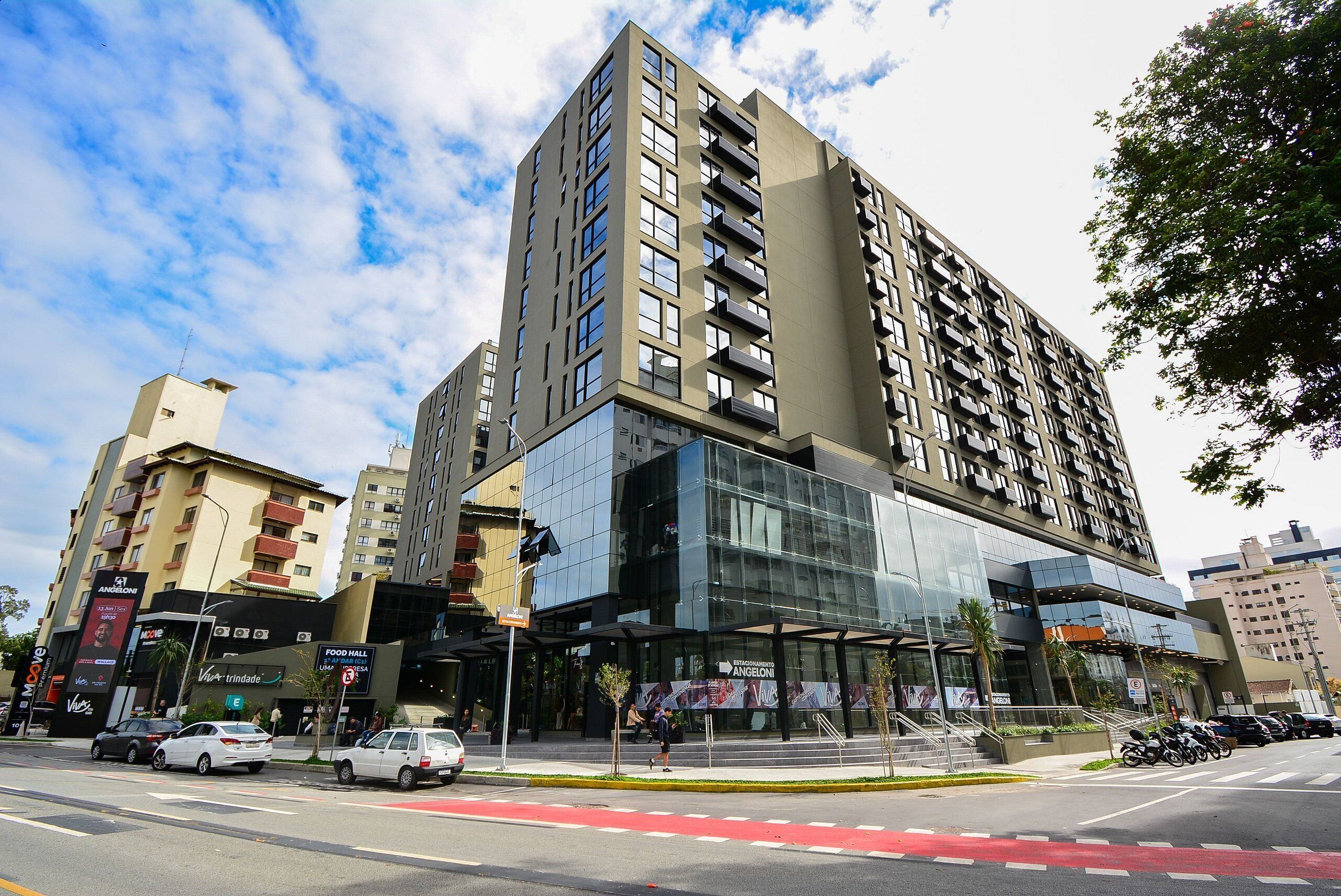 Um edifício moderno de vários andares com fachada de vidro, praça de alimentação e entrada acessível com rampa.