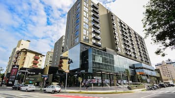 Um edifício moderno de vários andares com fachada de vidro, praça de alimentação e entrada acessível com rampa.