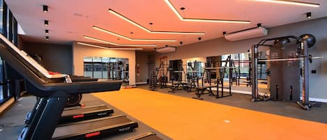 Et moderne fitnesscenter med løbebånd, styrkemaskiner og et stort spejl.