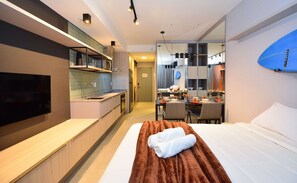 Quarto de hotel moderno com uma cama grande, televisão, cozinha compacta e área de refeições.