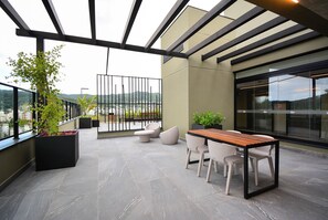 Terraço moderno ao ar livre com área de jantar, assentos e plantas em vasos.