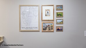 A wall with framed artwork including a map of Wilmington, North Carolina, and various other framed pictures.