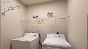 A laundry room with two front-loading washing machines, a drying rack, and a shelf with laundry supplies.