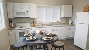 A compact kitchen with white cabinets, a microwave, a stove, and a dining area with a round table and stools.