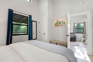 A bedroom with a bed, a bench, a door, and a window.