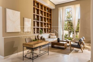 A modern living room with a sofa, coffee table, and chairs, a wooden bookshelf, and a large window with curtains. - Harbor NT2307 by Moikkarentals (Puerto Vallarta)
