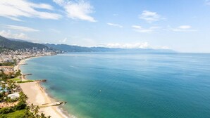 A coastal cityscape with a beach, clear blue sea, and distant mountains. - Harbor NT2307 by Moikkarentals (Puerto Vallarta)
