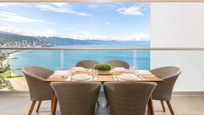 A dining table set for four with wicker chairs, overlooking a coastal view. - Harbor NT2307 by Moikkarentals (Puerto Vallarta)
