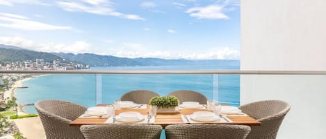 Une table à manger pour quatre personnes, avec des chaises en osier, donnant sur une vue sur la côte.