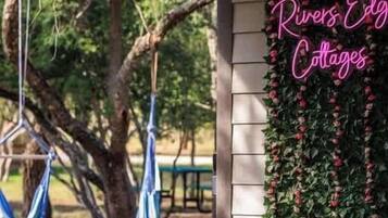 Eine Veranda mit einer Hängematte und einem Neon-Schild mit der Aufschrift 'Rivers Edge Cottages'.