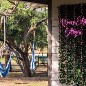 Une véranda avec un hamac et un panneau lumineux néon indiquant : « Rivers Edge Cottages ».