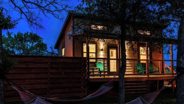 A wooden cabin with a porch, green chairs, and a hammock.