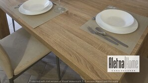 A modern kitchen with a dining table set for two, featuring a bottle of wine, a bowl of fruit, and white plates.