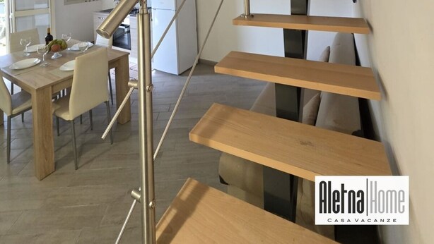 A modern interior with a wooden staircase, a dining area, and a kitchen.