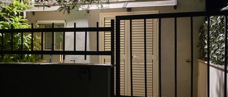 Une entrée fermée par un portail mène à une propriété dont la façade est blanche et qui possède un balcon.