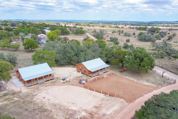 A rural property with two wooden cabins, a fenced riding arena, and surrounding trees.